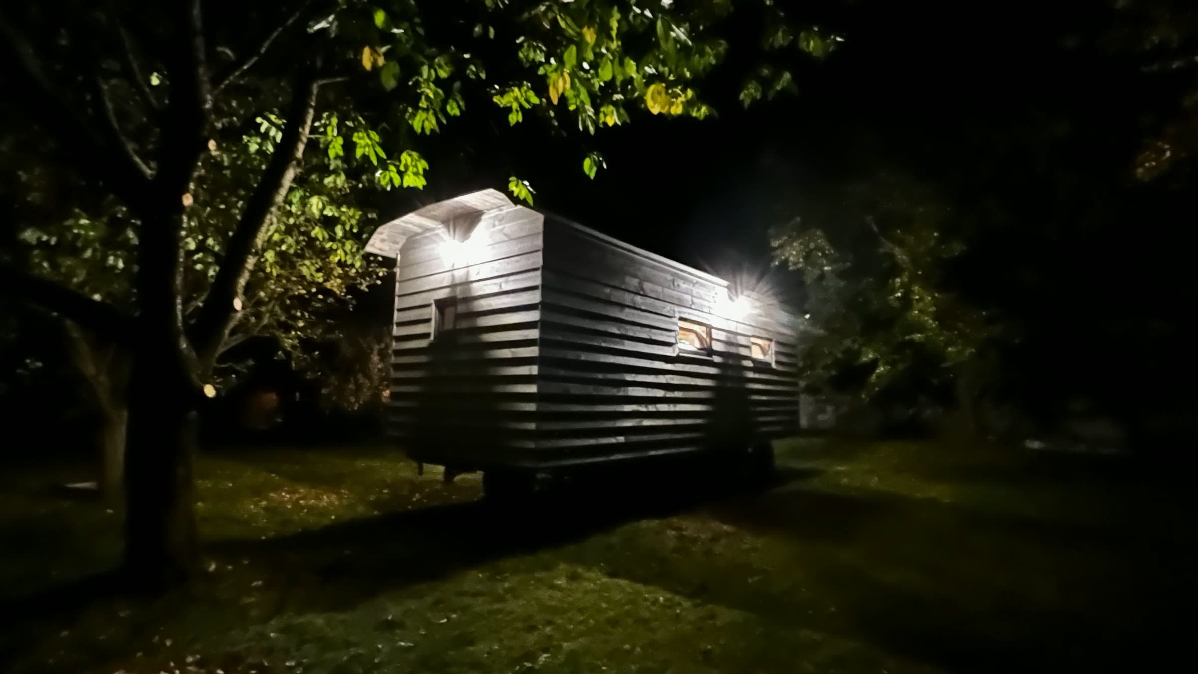 Maringotka v noci pod stromem, svítí venkovní lampy